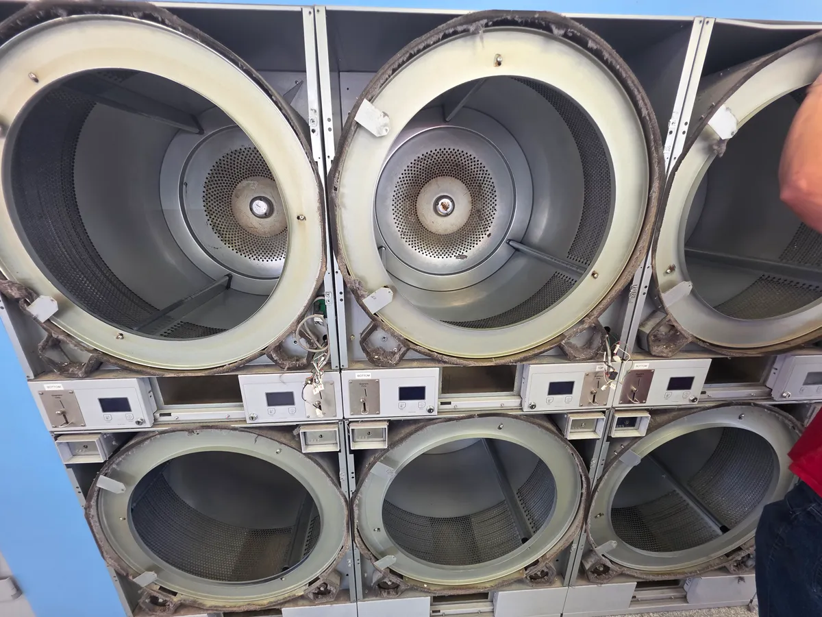 Stacked commercial dryers with their doors removed for cleaning